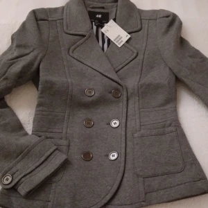 HELT NY & OANVÄND Grå höstjacka / kavaj i tjock mjuk bomull. Strlk: 36 / SMALL. - Fin grå jacka/kavaj i skepparkavaj-stil med fina sömmar vid axlarna, tillverkad i tjockare men mjukt sweatshirtliknande bomullstyg, perfekt för tex höst eller vår. Storlek: 36/SMALL, men passar troligen även någon med 34/XS. Tags sitter kvar sedan inköpet