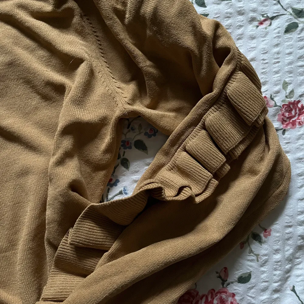 En finstickad mörkbeige tröja med populär volangdetalj från H&M. Helt i nyskick, utan defekter, i storlek 34. Frakt tillkommer💕. Stickat.