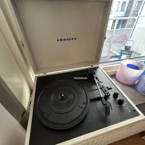 Vit skivspelare från Crosley - Säljer en stilren vit skivspelare från Crosley. Den har en klassisk design med inbyggda högtalare och en praktisk låda som skyddar skivspelaren när den inte används. Perfekt för att spela dina favoritvinylskivor hemma. Den har även bluetooth.