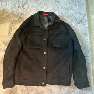 Svart jacka med knappar - Säljer en stilren svart jacka med knappar framtill och två stora bröstfickor. Jackan har en klassisk krage och långa ärmar, perfekt för en cool och avslappnad look.
