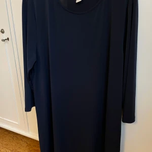 Mörkblå klänning från H&M - Säljer en stilren mörkblå klänning från H&M Basic. Klänningen har en enkel design med långa ärmar och en rund halsringning. Perfekt för en minimalistisk look.