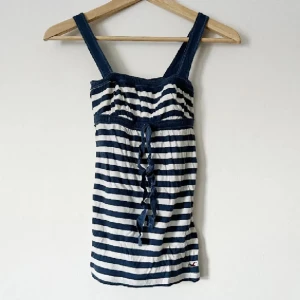 Randig linne från Hollister - Säljer ett randigt linne från Hollister i blått och vitt. Linnet har breda axelband och en knytning framtill. Perfekt för sommardagar! Storlek S (XS)