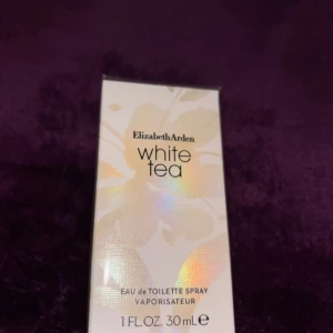 Parfym från Elizabeth Arden - Elegant parfymflaska från Elizabeth Arden med doften White Tea. Flaskan är fyrkantig med en vit och guldig kork, och har en stilren design i vitt och guld. Perfekt för den som älskar fräscha och lätta dofter.