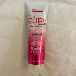Sulfatfritt schampo med moringaolja från The Curl Company - Säljer ett sulfatfritt schampo från The Curl Company, perfekt för lockigt och vågigt hår. Innehåller närande moringaolja som hjälper till att återfukta och definiera lockarna. Förpackningen är 250 ml och har en snygg rosa och vit design.