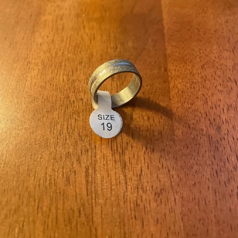 Elegant silverfärgad ring i storlek 19. Den har en stilren och modern design som passar perfekt för både vardag och speciella tillfällen.. Asusteet.