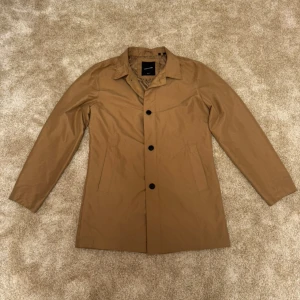 Beige rock från Jack & Jones - Snygg brun jacka från Jack & Jones Premium. Jackan har en klassisk krage och knäppning framtill med svarta knappar. Perfekt för en stilren och sofistikerad look.  Kön: Herr Storlek: M Skick: 9/10 Ord: pris: 399 SEK  Din stil: spara inlägget så du inte missar denna kappa Inte din stil: Kolla min profil. Du kommer hitta något för alla kön och åldrar.