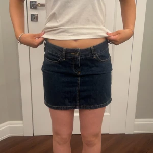 Mörkblå jeanskjol - Snygg mörkblå jeanskjol med klassisk femficksdesign och knappgylf. Kjolen har en kort längd och en liten slits baktill för extra rörelsefrihet. Perfekt för en avslappnad stil.