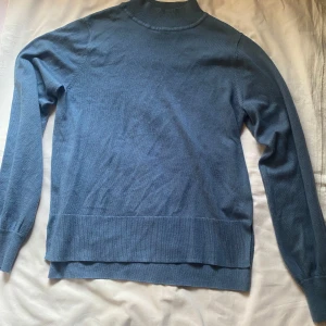 Blå polotröja - Säljer en stilren blå polotröja med långa ärmar. Perfekt för kyligare dagar och enkel att matcha med olika outfits. Tröjan har en klassisk design med ribbade kanter vid ärmslut och nederkant.