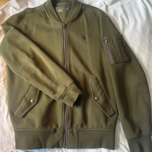 Olivgrön Tröja med dragkedja från Ralph Lauren - Säljer en snygg olivgrön bomberjacka från Ralph Lauren. Jackan har dragkedja framtill och en broderad logga på bröstet. Den har långa ärmar och praktiska fickor med knappar. Perfekt för en stilren look! Skick 9/10. Nypris ca 2400.                  https://www.zalando.se/polo-ralph-lauren-long-sleeve-troeja-med-dragkedja-company-olive-po222s0bz-n11.html