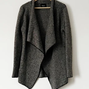 Grå mönstrad jacka från Zara - Snygg grå kofta från Zara med ett klassiskt fiskbensmönster. Den har en öppen design utan knappar och långa ärmar. Perfekt för höst och vår när du vill ha en stilren look. Storlek S.