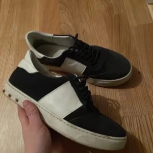 Svartvita sneakers med snörning - Snygga svartvita sneakers med snörning och en stilren design. Skorna har en vit sula och svart ovandel med vita detaljer. Perfekta för en casual look.