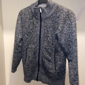 Grå stickad kofta med dragkedja - Säljer en mysig grå stickad kofta med dragkedja. Perfekt för kyliga dagar med sin långa ärmar och bekväma passform. Ett måste i garderoben för den som älskar stil och komfort.