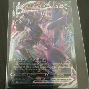 Grimmsnarl VMAX Pokémonkort - Säljer ett Grimmsnarl VMAX Pokémonkort med 330 HP. Kortet har en färgglad och glittrig design med G-Max Drill attack. Perfekt för samlare eller spelare som vill förstärka sin kortlek.