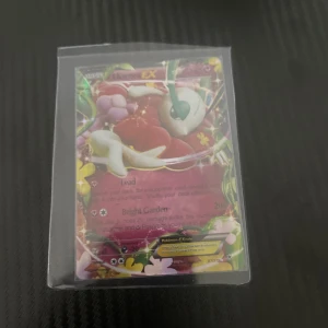 Pokémon-kort Mega Venusaur EX - Säljer ett Pokémon-kort av Mega Venusaur EX. Kortet har en färgglad design med blommor och glänsande detaljer. Perfekt för samlare eller spelare som vill förstärka sin kortlek.