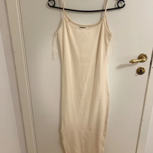 Beige ärmlös klänning - Snygg beige klänning med smala axelband och en enkel design. Perfekt för en stilren look. Klänningen är ärmlös och har en kroppsnära passform. Dock har klänningen en liten liten fläck vid sidan av känningen dock syns knappt!