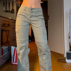 Gröna/beiga cargobyxor - Snygga gröna cargobyxor med flera fickor och en loose passform. Byxorna har en knapp och dragkedja framtill och är perfekta för en avslappnad stil. De är högmidjade och tillverkade i ett slitstarkt material.