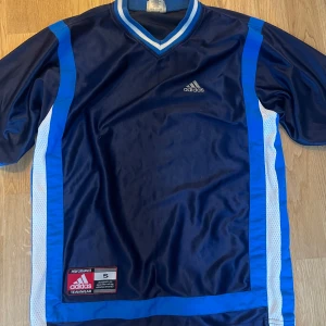 Blå T-shirt Adidas - Snygg blå tshirt från Adidas. Tröjan har en V-ringning och Adidas-loggan på bröstet. 