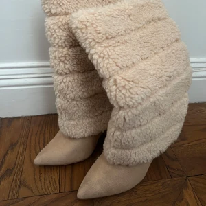 Beige pälsboots med klack - Snygga beige boots med en mjuk och fluffig pälsdesign. De har en spetsig tå och en stabil klack som ger en elegant look. Perfekta för att hålla sig varm och stilren under kyliga dagar. Använda 1 gång.