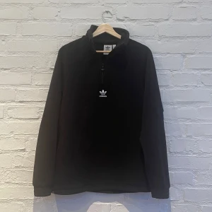 Svart fleece tröja från Adidas - Säljer en svart fleece tröja från Adidas med dragkedja och det klassiska logotypen på bröstet och ryggen. Perfekt för kyliga dagar. Tröjan har långa ärmar och en hög krage för extra värme. Passar bra till både vardag och sportiga aktiviteter.