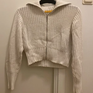 Vit stickad kofta från Gina Tricot - 💕Säljer en snygg vit stickad kofta från young Gina Tricot. Koftan har en dragkedja framtill och en hög krage. Den är ribbad vid ärmslut och nederkant, vilket ger en skön passform. Perfekt för kyliga dagar!💕