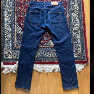 Slim Fit Nudie Dry/ Raw denim Grim Tim  - Dry/ raw Nudie Jeans i slim fit modellen Grim Tim. Tillverkade i 98% bomull och 2% elastan.  Storlek 31x32