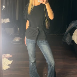 Svart t-shirt med bälte - Säljer en svart t-shirt med korta ärmar och ett bälte i midjan. Perfekt för en stilren och avslappnad look. Passar bra till jeans eller kjol.