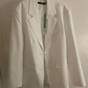 Vit kavaj från Gina - Elegant vit kavaj från ginq med klassisk design. Kavajen har två knappar framtill och fickor med lock. Perfekt för en stilren look. Passar bra till både formella och avslappnade tillfällen. Aldrig använd lapp finns kvar