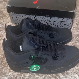 Black Cats (Svarta Nike Air Jordans 4) - Snygga svarta Nike Air Jordans med klassisk design och snörning. Skorna har en stilren look med diskreta detaljer och är perfekta för sneaker-entusiaster.