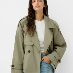 Olivgrön trenchcoat - Snygg olivgrön trenchcoat med dubbelknäppning och breda slag. Jackan har en oversized passform och långa ärmar med knappar vid ärmsluten. Perfekt för en stilren look.