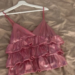 Rosa glittrig volangtopp - Säljer en rosa glittrig topp med volanger och smala axelband. Perfekt för en festlig kväll 