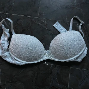 Vit spets-bh - Elegant vit bh med spetsdetaljer och vadderade kupor. Justerbara axelband för perfekt passform. Ej använd utan bara tagit bort lappen på produkten!!