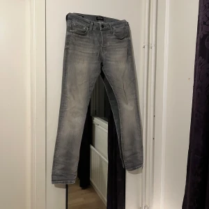 Jack and Jones jeans  - Snygga grå jeansbyxor med en klassisk femficksdesign och knappgylf. Perfekta för en avslappnad stil. De har en lätt tvättad look som ger en cool och trendig känsla.