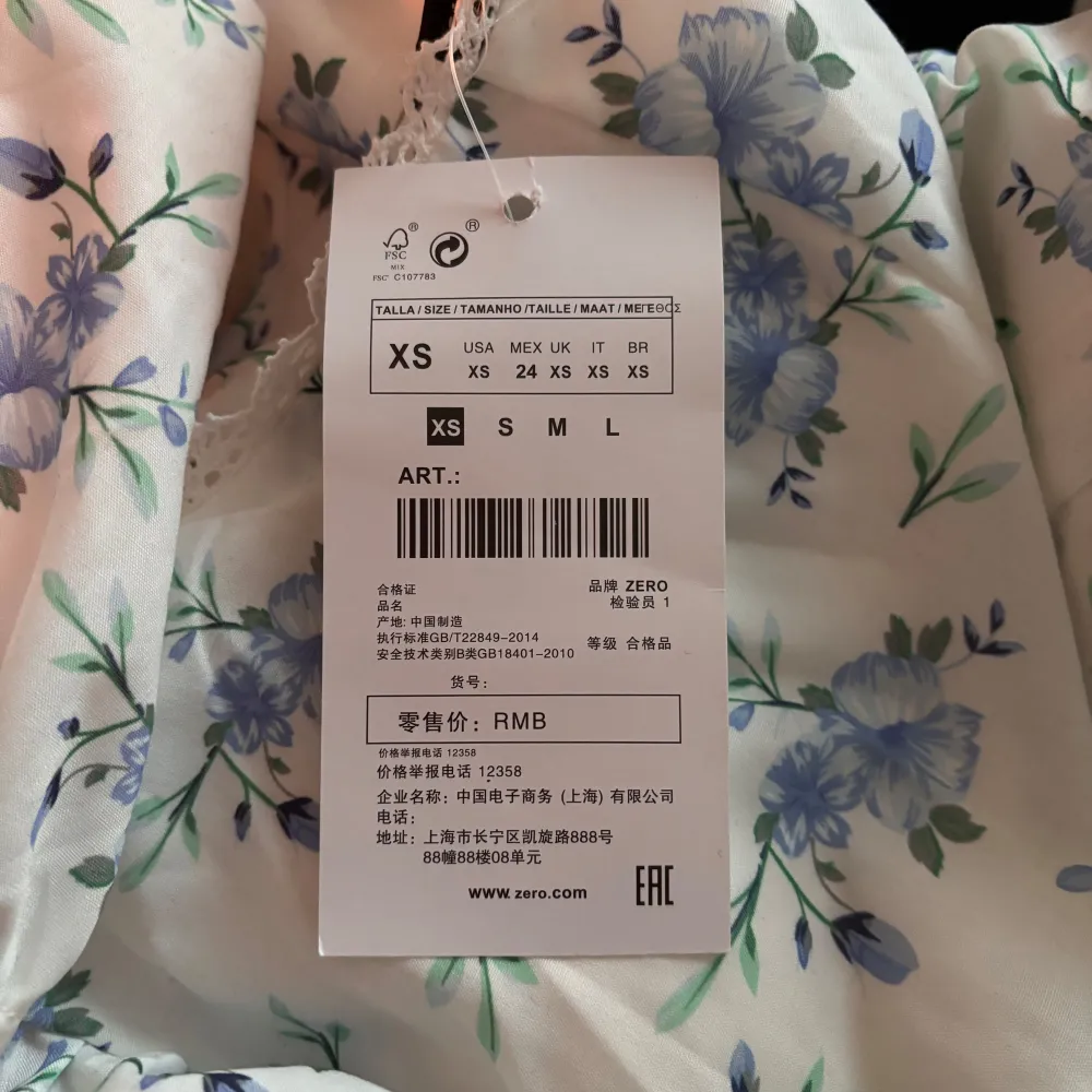 Charmig kortklänning med blommigt mönster i blått och grönt på vit botten. Klänningen har en v-ringad hals och korta ärmar med volangdetaljer. Dragkedja på sidan, ej använd och prislapp sitter kvar. Passar som både XS och XXS.. Mekot.