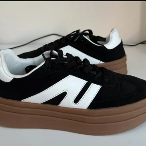 Svartvita sneakers med brun sula - Snygga svartvita sneakers från Shone med en kontrasterande brun sula. Skorna har en klassisk design med snörning och en vit detalj på sidan. Perfekta för en avslappnad stil.