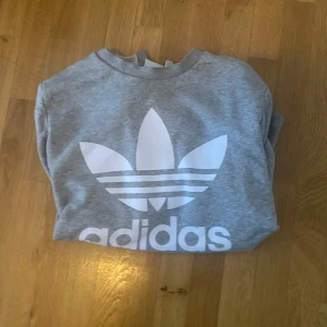 Grå sweatshirt från Adidas - Säljer en grå sweatshirt från Adidas med det klassiska trefoil-logotypen i vitt på framsidan. Tröjan har en rund hals och är perfekt för en avslappnad stil. Passar bra till både jeans och träningsbyxor. 158. 40kr. Priset går att diskuteras 