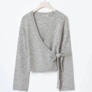 Grå omlottkofta med knytband - Säljer en mysig grå omlottkofta med knytband i sidan. Koftan har långa ärmar och en mjuk, stickad textur som passar perfekt för kyligare dagar. Perfekt för en avslappnad och stilren look. Endast använd 2 gånger och är i nyskick😊