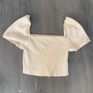 Vit ribbad topp med puffärmar - Säljer en söt vit ribbad topp med puffiga kortärmar. Toppen är croppad och har en stilren design som passar perfekt för varmare dagar.