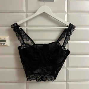 Svart spets linne/topp från nakd. Storlek:XL.  - Snygg svart korsett med spetsdetaljer och breda axelband. Perfekt för en elegant look med en touch av romantik. Den har en vacker spetsdesign som ger en feminin känsla. Aldrig använd och aldrig testad. Storlek:XL. Säljer för 175 kronor 