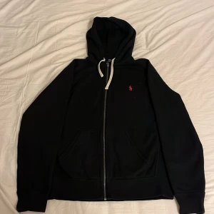  zip hoodie Polo Ralph Lauren - Säljer en svart hoodie från Polo Ralph Lauren med dragkedja och luva. Säljer för att den inte passar mig längre och har använt 1 gång. Väldigt snygg och inga defekter precis som ny.