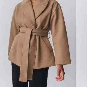 Beige kappa med bälte - Snygg beige kappa med knytbälte i midjan och bred krage. Perfekt för höst och vår. Den har en elegant och stilren design med långa ärmar. Använd fåtal tillfällen. Slutsåld.🤍