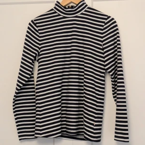 Randig turtleneck tröja från Holly & Whyte - Snygg randig tröja i svart och vit från Holly & Whyte by Lindex. Tröjan har en dragkedja i halsen och långa ärmar, perfekt för en stilren look.