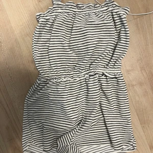 Randig ärmlös jumpsuit från Zara - Säljer en söt och bekväm ärmlös jumpsuit från Zara i svart och vit randigt mönster. Perfekt för varma dagar med sin elastiska midja och mjuka material. Passar storlek 152.
