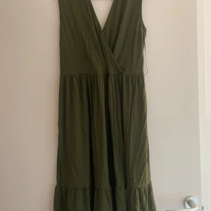 Olivgrön klänning från Bodyflirt - Snygg olivgrön klänning från Bodyflirt med omlott-design och spetsdetaljer på axelbanden. Perfekt för en somrig look med sin luftiga passform och v-ringning.