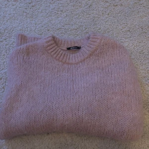 Rosa stickad tröja från Vero Moda - Mysig rosa stickad tröja från Gina. Perfekt för kyliga dagar med sin mjuka och varma känsla. Tröjan har långa ärmar och en rund halsringning. Den är stor i storleken