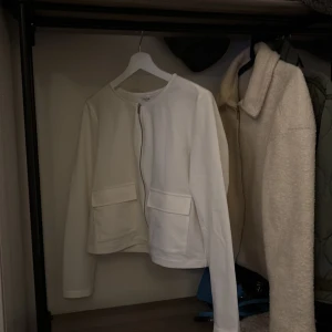 Vit jacka från Pieces - Säljer en stilren vit jacka från Pieces i storlek M. Jackan har en dragkedja framtill och två fickor. Perfekt för en minimalistisk look.