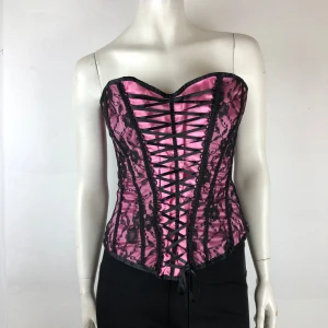 Rosa korsett med svart spets - Snygg rosa korsett med svart spetsdetalj och snörning fram och bak. Axelbandslös design som ger en elegant look. Perfekt för en festlig kväll. Storlek M. Ej underklädeskorsett.