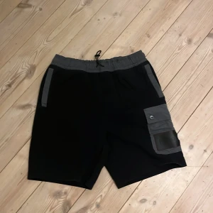 Svarta shorts från Hugo - Snygga svarta shorts från Hugo med grå detaljer och elastisk midja. Perfekta för en avslappnad stil med praktiska fickor och en cool design. Är öppen för bud