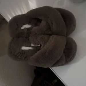 Bruna fluffiga tofflor - Mysiga bruna tofflor med fluffigt material som ger en varm och bekväm känsla. Perfekta för att hålla fötterna varma under kyliga dagar.