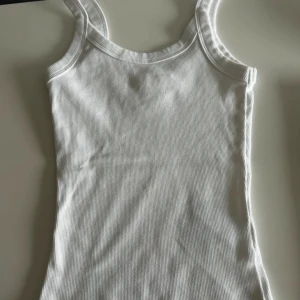 Vit ribbad linnetopp från Gina Tricot - Säljer en supersnygg vit ribbad topp från Gina Tricot i storlek XXS. Använd endast ett fåtal gångger. Perfekt som ett basplagg i garderoben. Toppen har breda axelband. 