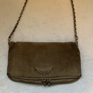 Rock Suede Clutch Zadig & Voltaire - Skitsnygg Zadig väska i brun mocka. Välanvänd med slitningar (se bild 2-4), men det ger den bara en skitnajs vintage-look. Nypris cirka 2900kr. Både kort och långt band tillkommer.